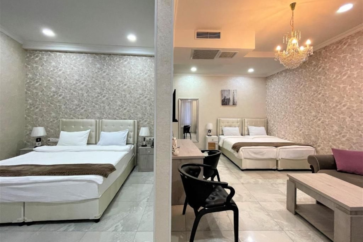 Quarto de hotel com cama, mesas de cabeceira, uma poltrona, escrivaninha e lustre.