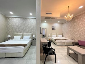 Quarto de hotel com cama, mesas de cabeceira, uma poltrona, escrivaninha e lustre.