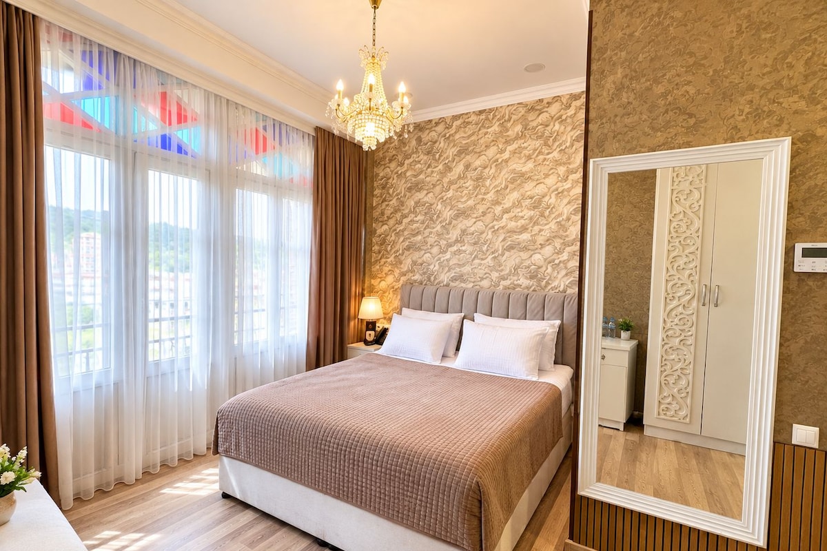 Quarto de hotel com uma cama grande, um lustre, um guarda-roupa e um espelho.