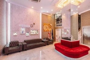 Um hall com um sofá vermelho, um sofá marrom e um candelabro.