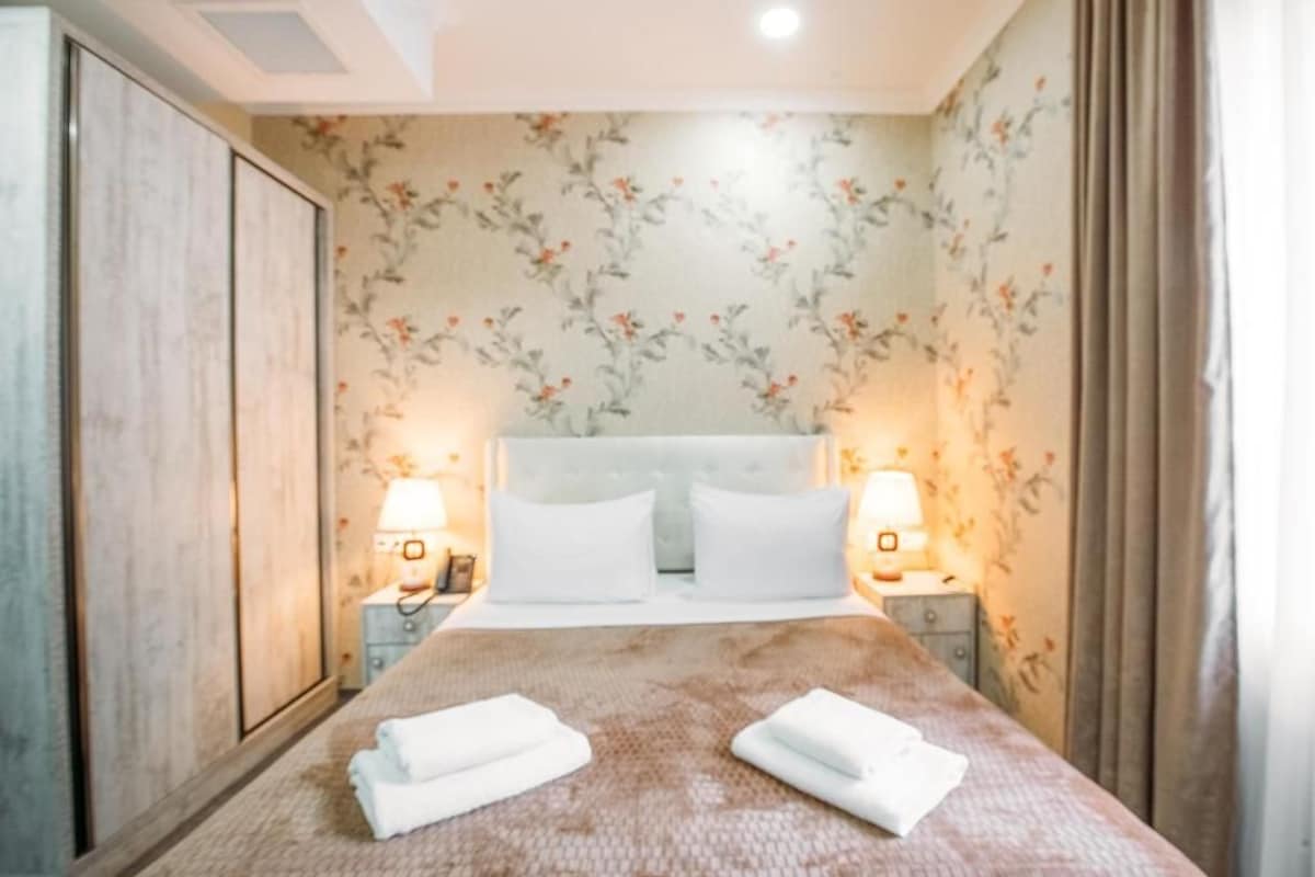 Quarto de hotel com cama, duas luminárias de cabeceira, mesa de cabeceira e guarda-roupa.