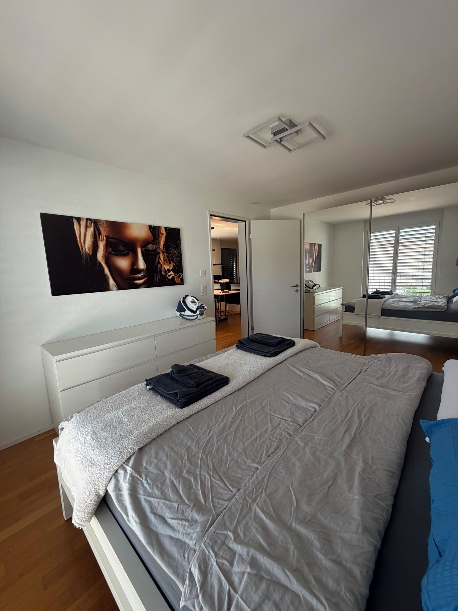 A modern bedroom with a large bed, a white dresser, and a painting on the wall.