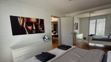 A modern bedroom with a large bed, a white dresser, and a painting on the wall.