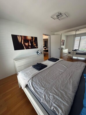 A modern bedroom with a large bed, a bedside table, a wall-mounted artwork, and a door leading to another room. - New Listing (dulliken)