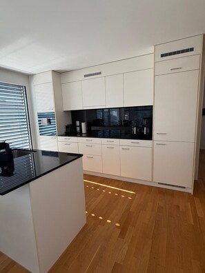 A modern kitchen with white cabinets, a black countertop, and a wooden floor. - New Listing (dulliken)