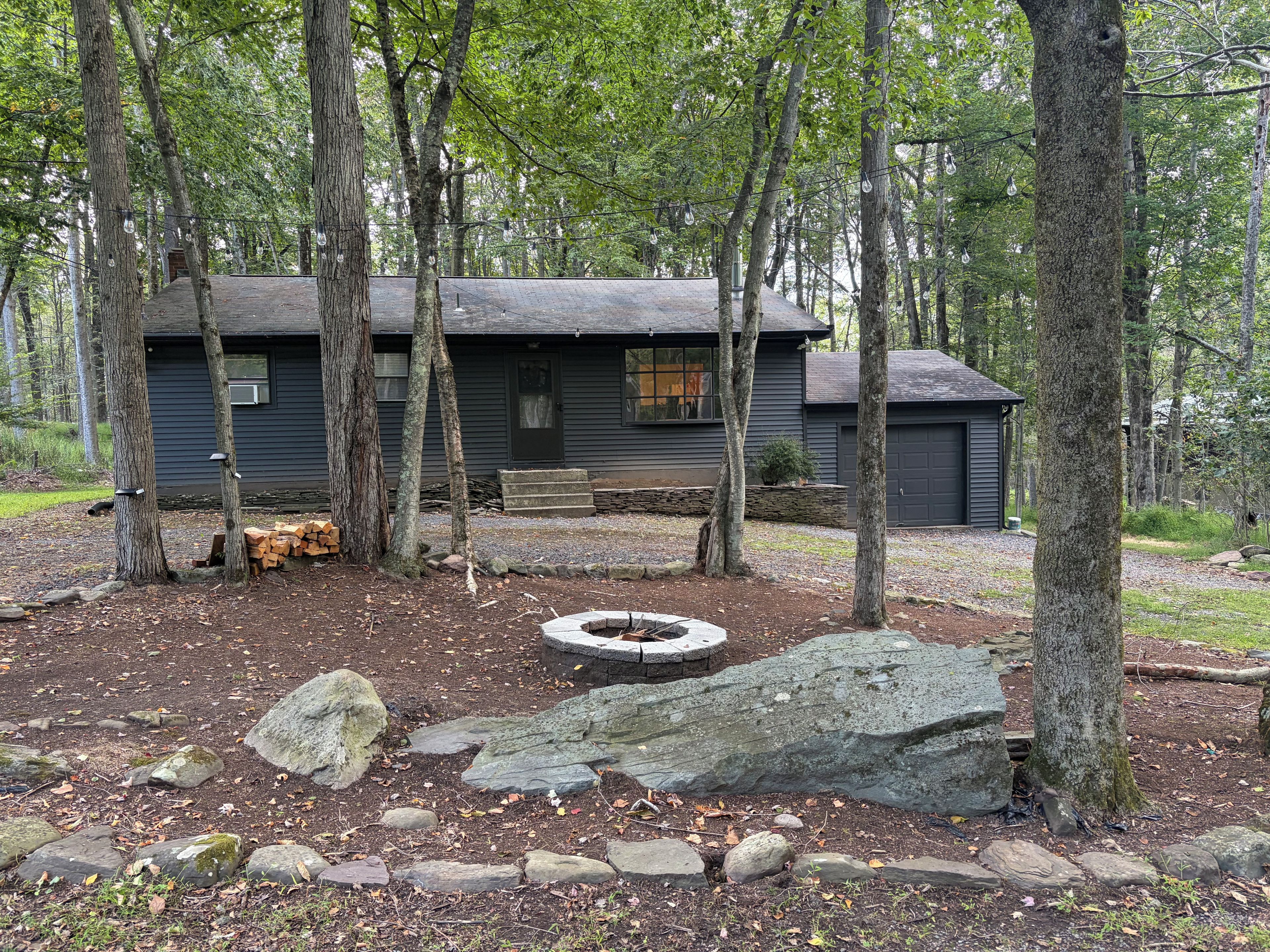 A cabin with a stone fire pit surrounded by rocks and trees.