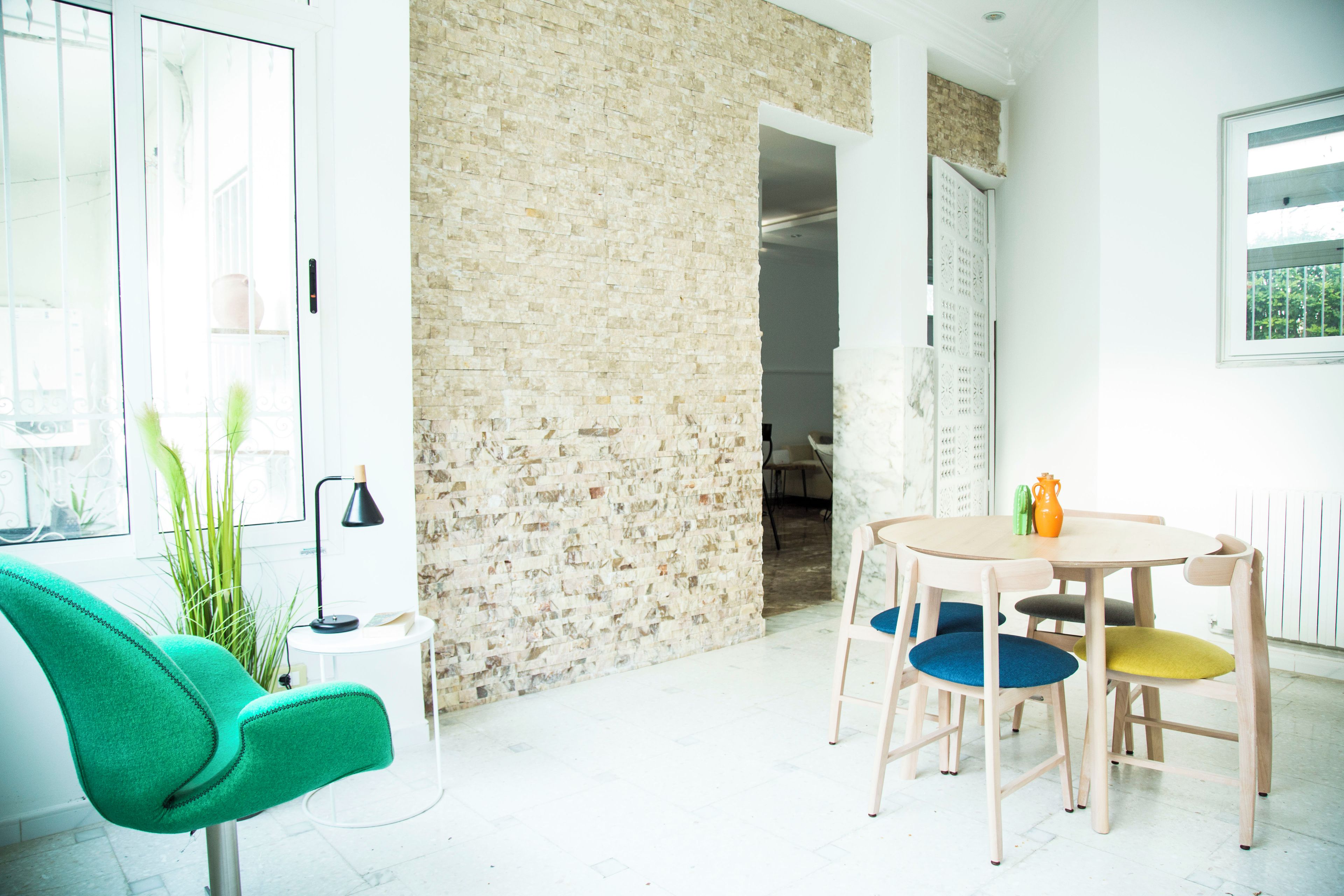 A modern interior with a brick wall, a round table with chairs, a green armchair, and a small side table with a lamp.