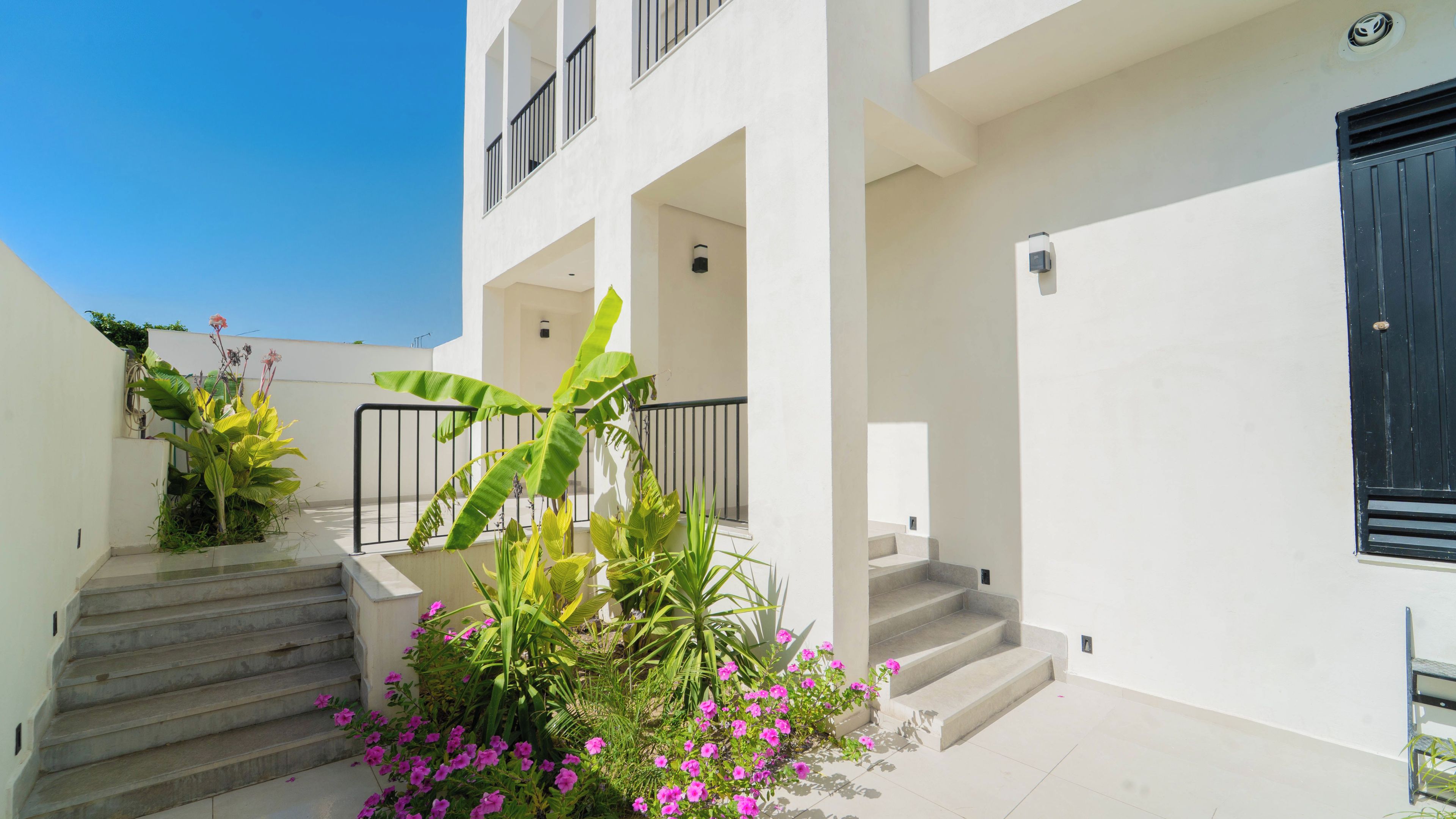 A residential building with a white exterior, a balcony with a black railing, and a staircase leading to the entrance.