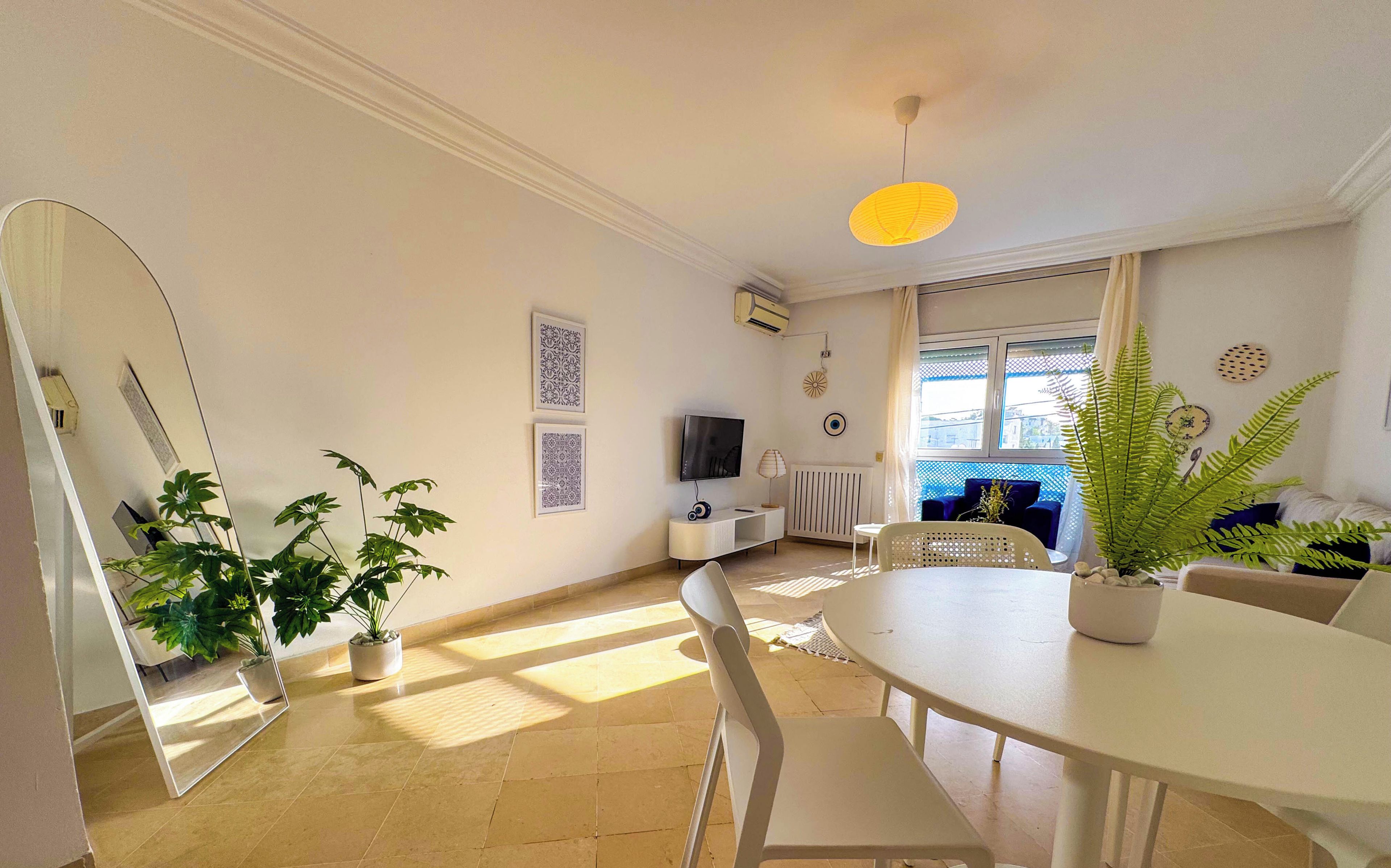 Una sala de estar moderna con una mesa de comedor, sillas, televisor y elementos decorativos.