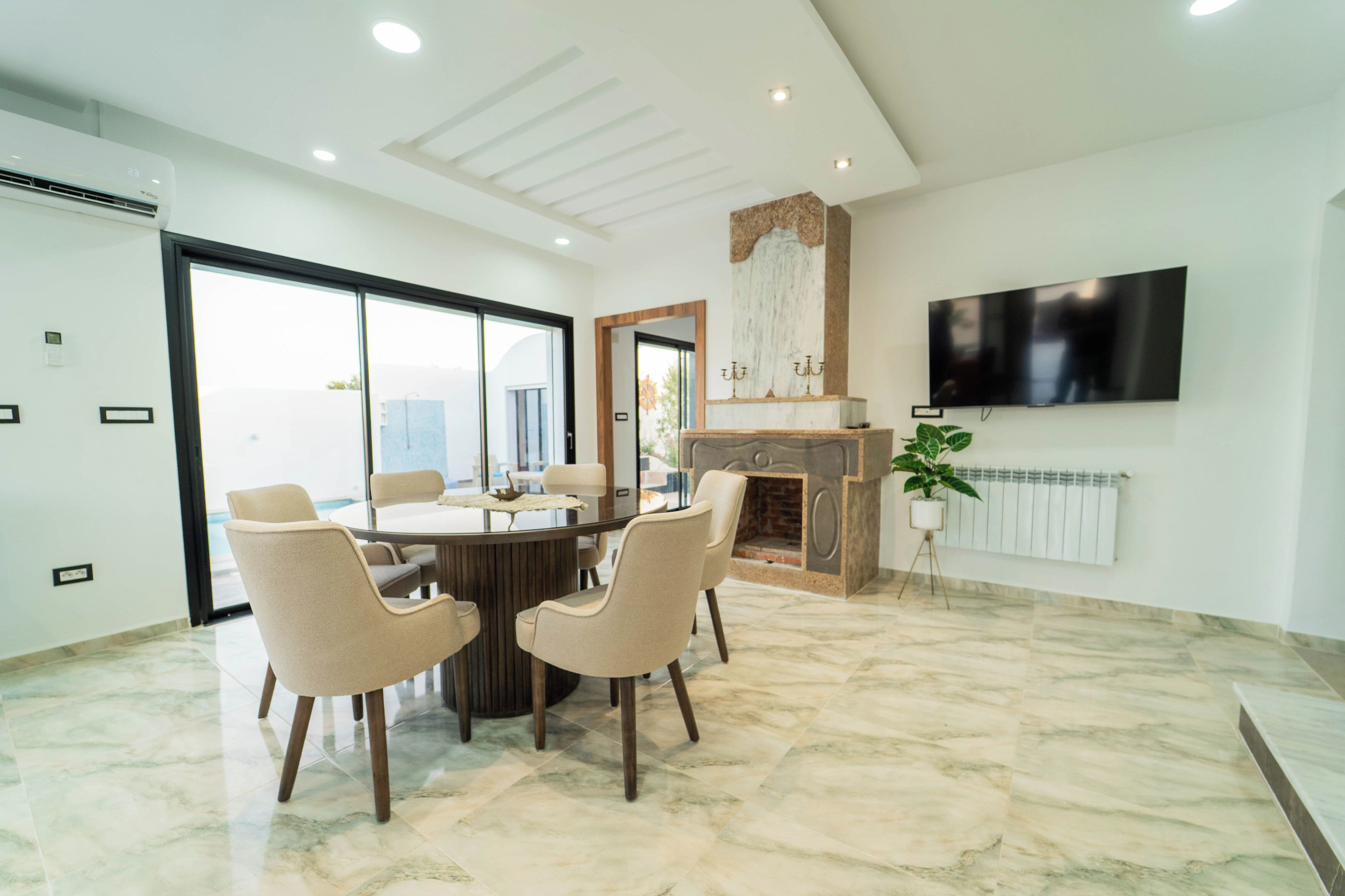Un comedor moderno con una mesa redonda, cuatro sillas, una chimenea y un televisor montado en la pared.