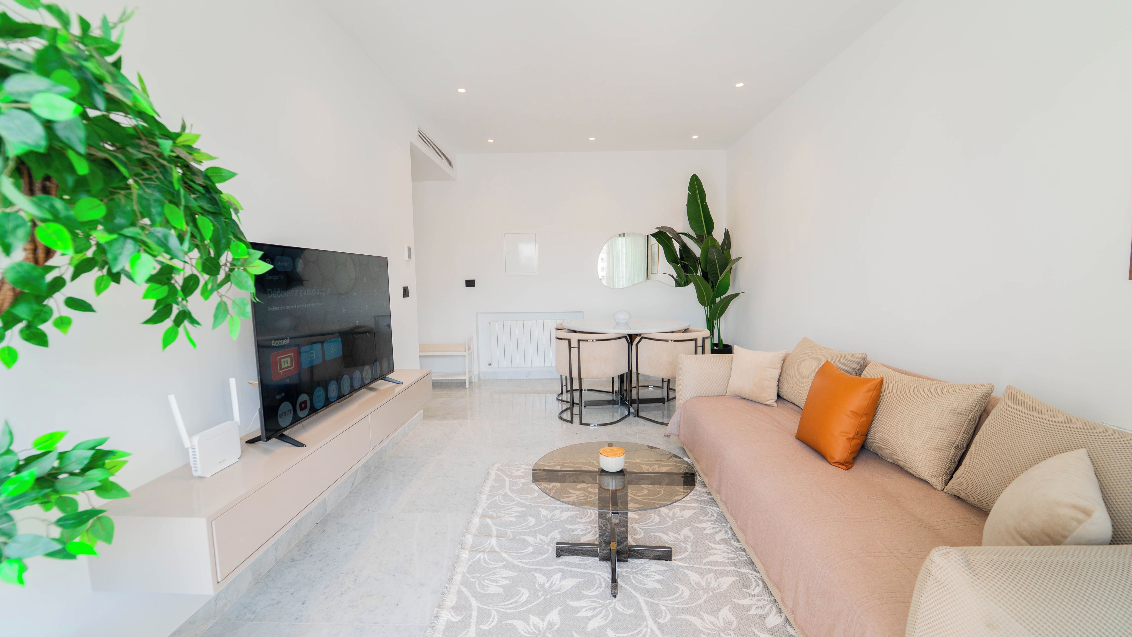 Ein modernes Wohnzimmer mit Flachbildfernseher, einer Couch, einem Couchtisch und einem Essbereich mit Tisch und Stühlen.