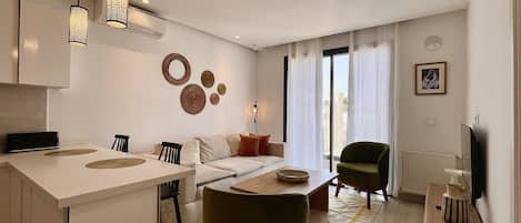 A modern living room with a sofa, a dining table, and a kitchen area.