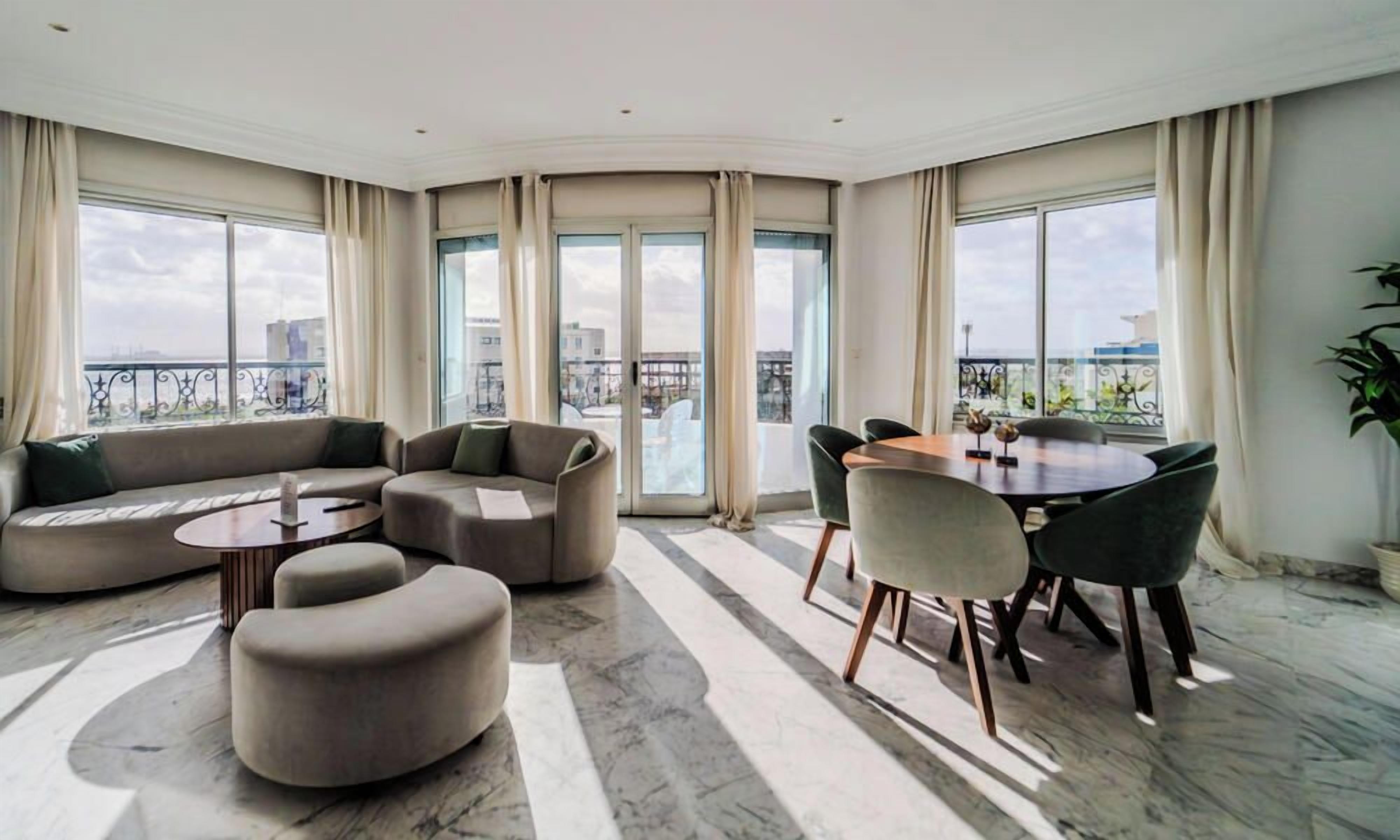 Amplia sala de estar con un sofá curvo, una mesa de comedor con sillas y ventanas grandes con vistas a la ciudad.