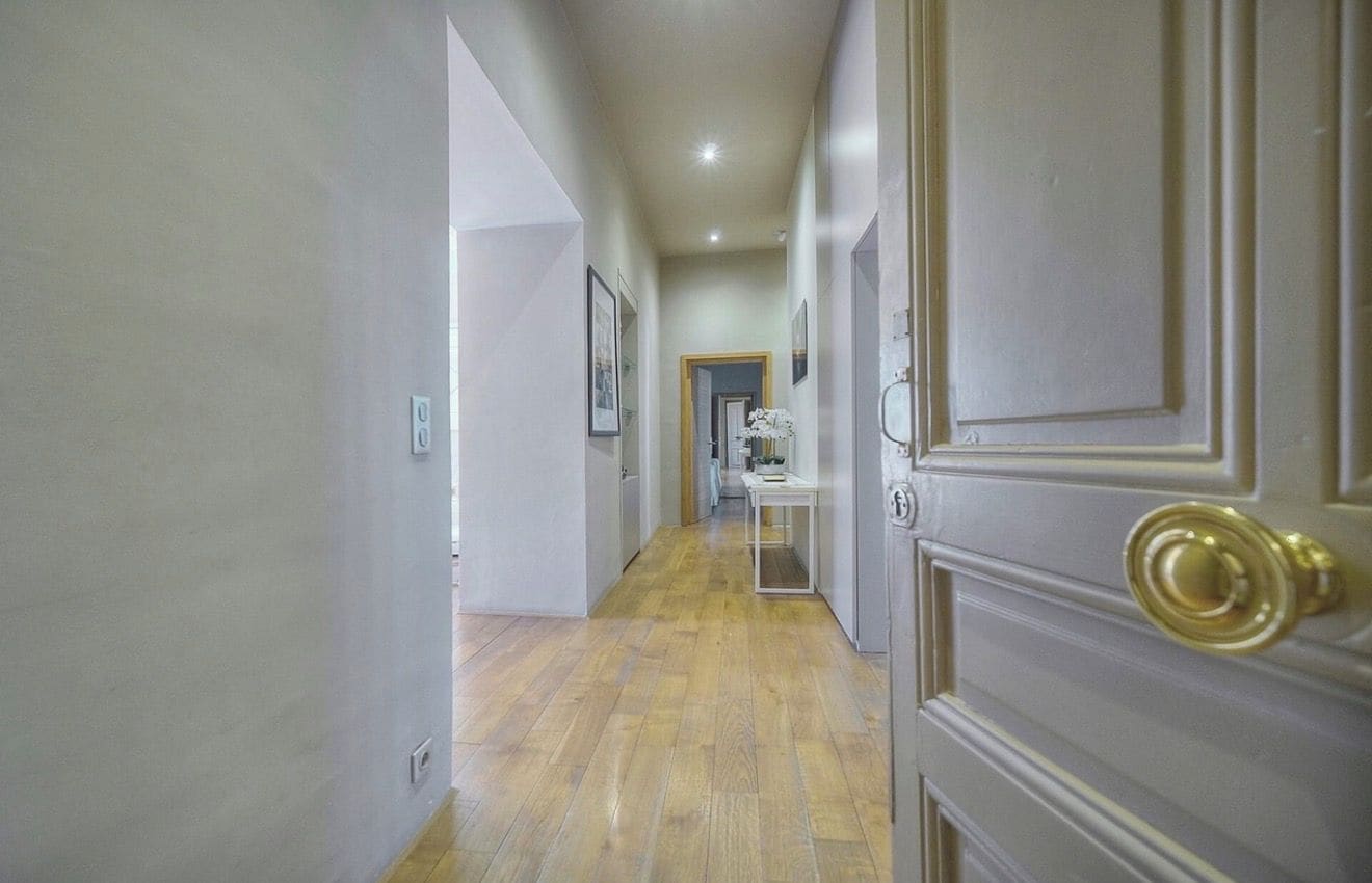 A hallway with wooden flooring, a door with a brass handle, and a framed picture on the wall.
