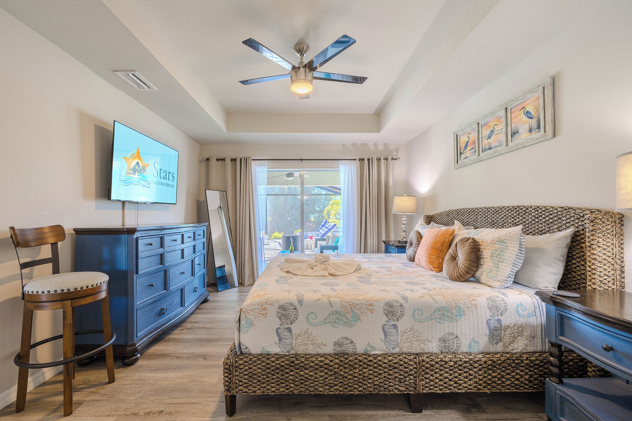 Quarto com cama, penteadeira, televisão, ventilador de teto e vista para o exterior.