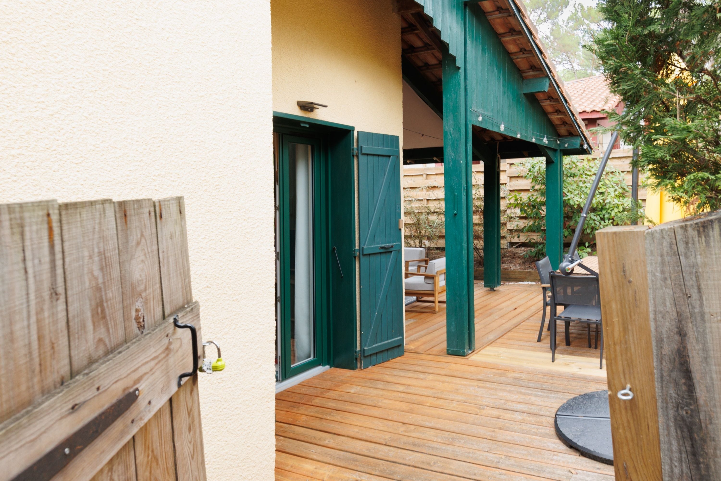 Une terrasse en bois dotée d’un espace salon couvert, d’une porte et d’un mur avec une fenêtre.