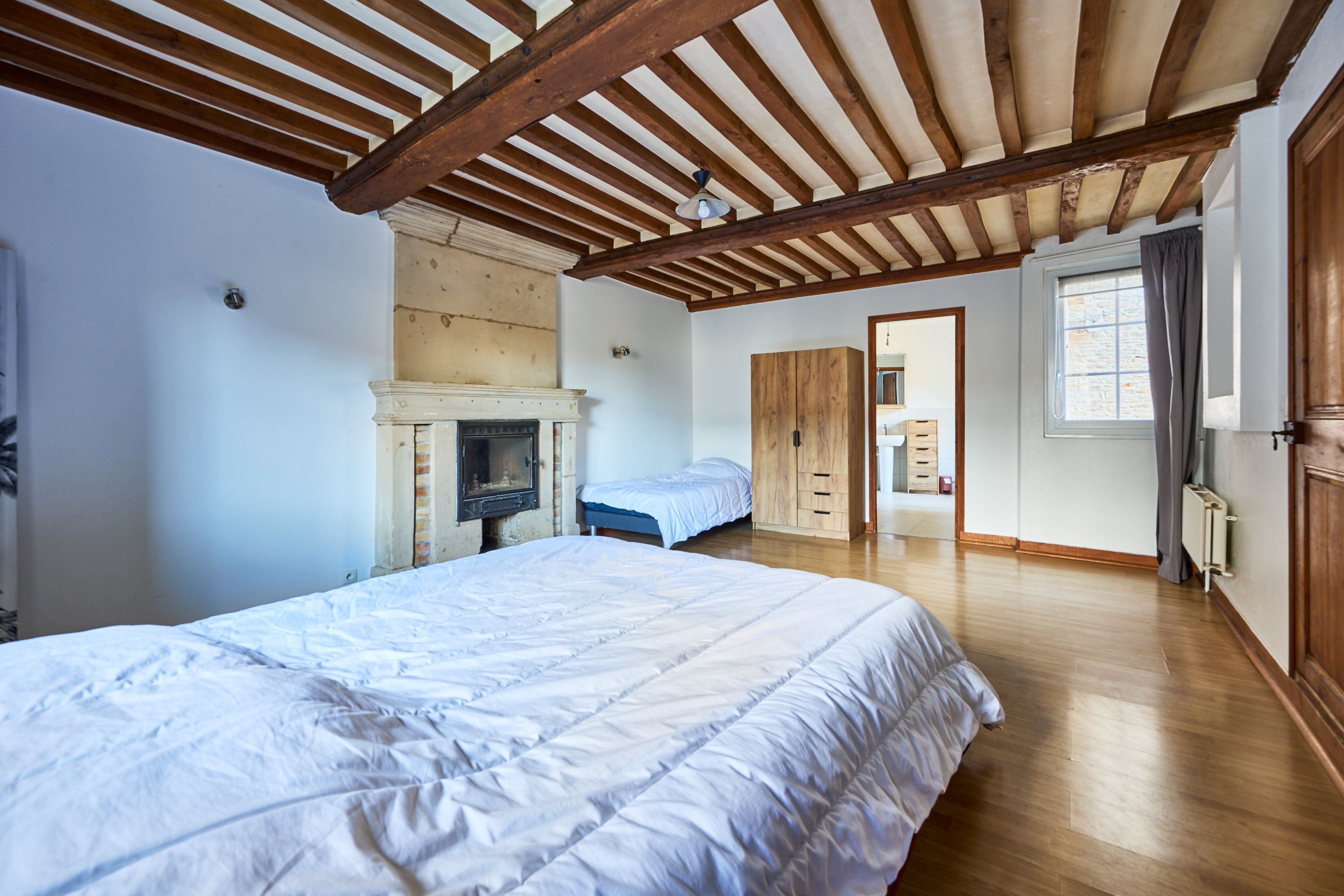 A bedroom with a large bed, a fireplace, wooden beams, and a view of the bathroom.