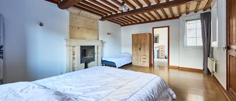 A bedroom with a large bed, a fireplace, wooden beams, and a view of the bathroom.