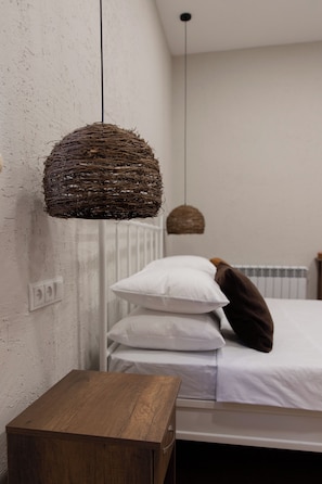 Un dormitorio con una mesita de noche de madera, una cama con ropa blanca y dos lámparas colgantes.
