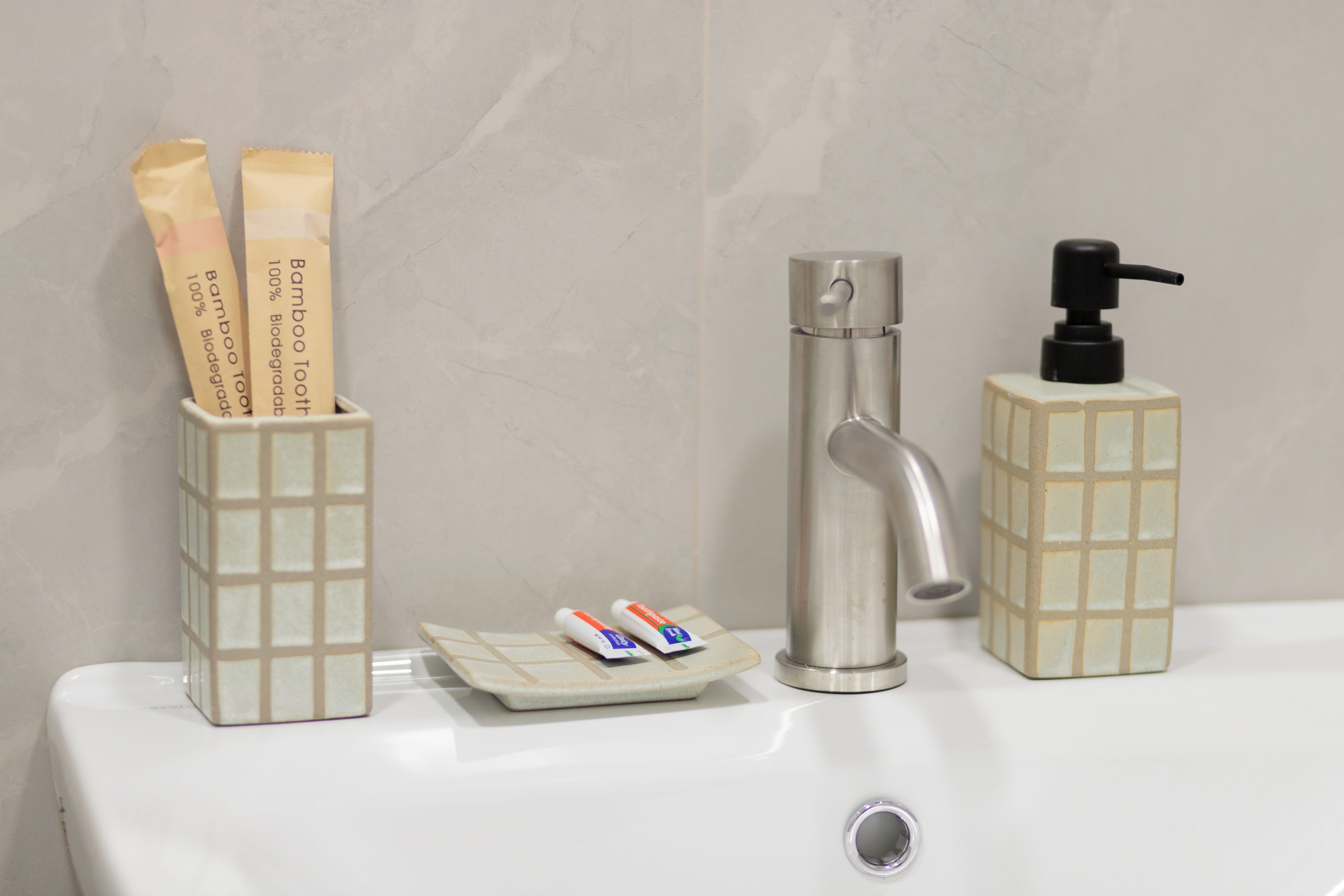 Un lavamanos de baño con una llave moderna, un dispensador de jabón y un porta cepillos de dientes con dos cepillos y dos tubos de pasta de dientes.