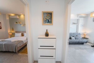 Una habitación de hotel moderna con una cama, un aparador, un cuadro y un sofá gris.