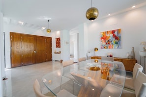 Un comedor moderno con una mesa de vidrio, sillas de madera e iluminación colgante.
