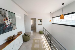 Un pasillo moderno con un cuadro abstracto de gran tamaño, una consola de madera, un bolso verde y una ventana con vistas.