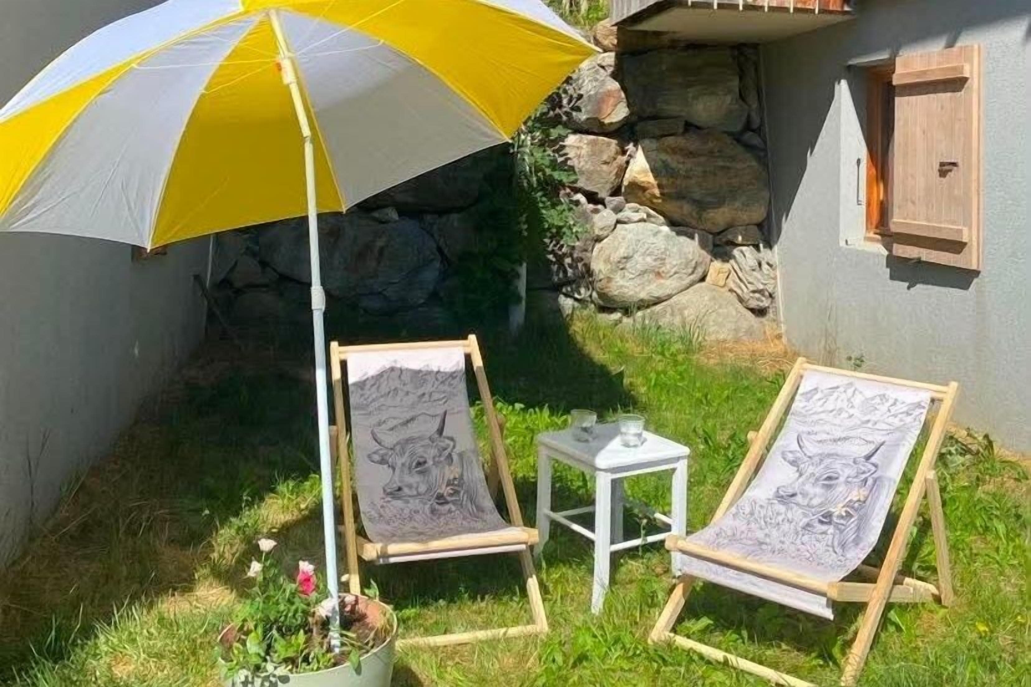 Two easels with canvases, a small table with a glass, and a yellow umbrella providing shade.
