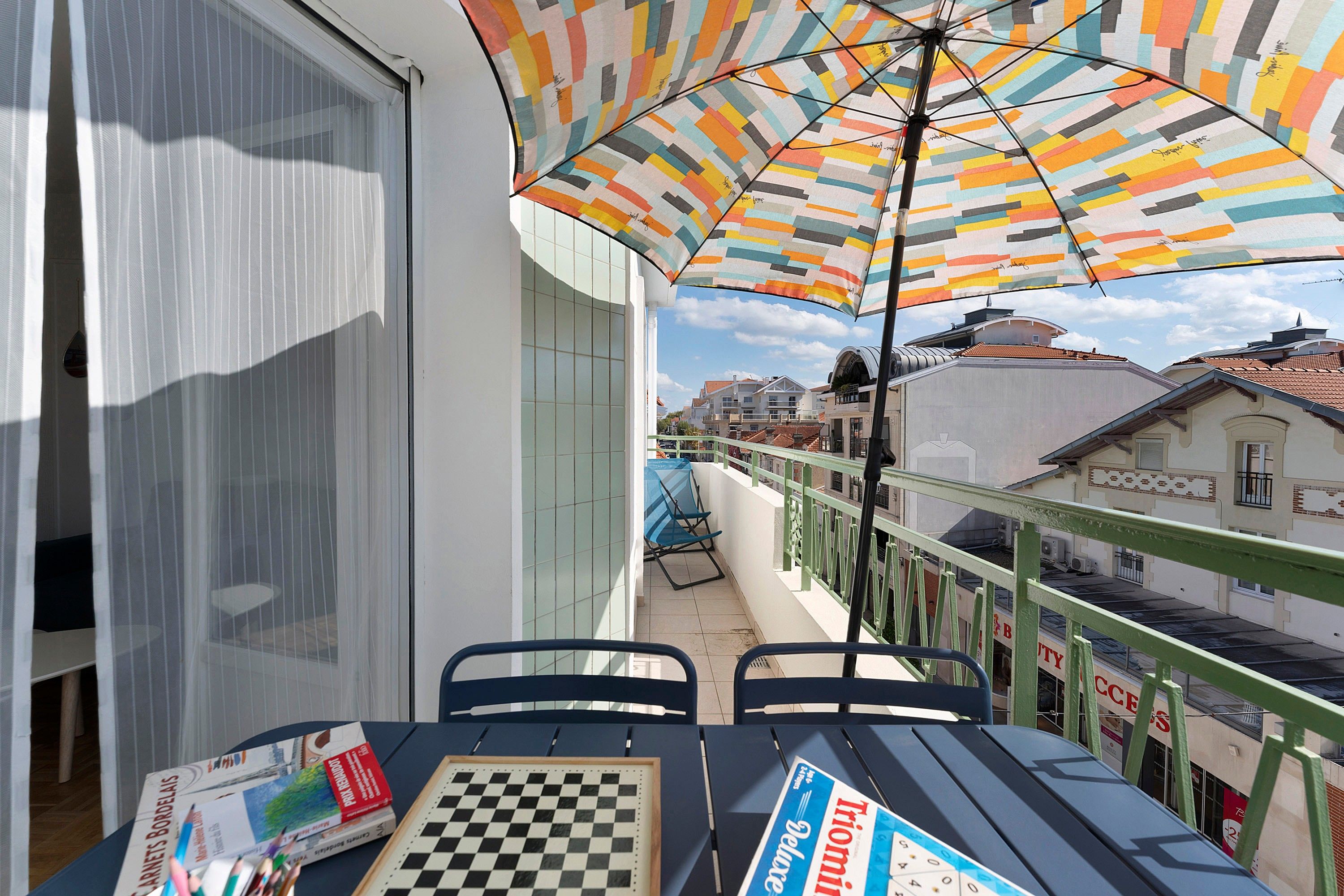 A balcony with a checkered table, chairs, and a colorful umbrella.