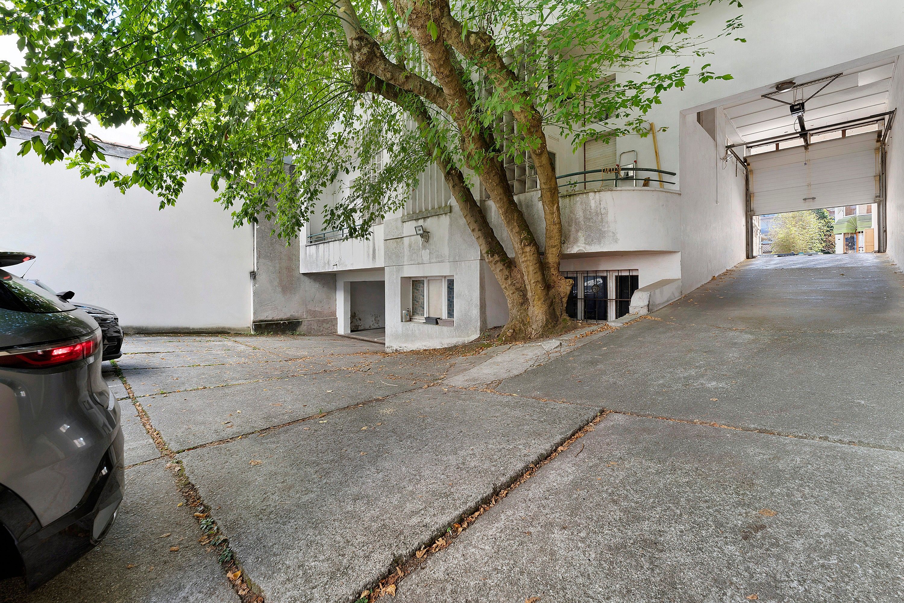 Ein Parkplatz mit einem Auto, einem Baum und einem Gebäude mit einer Garagentür.