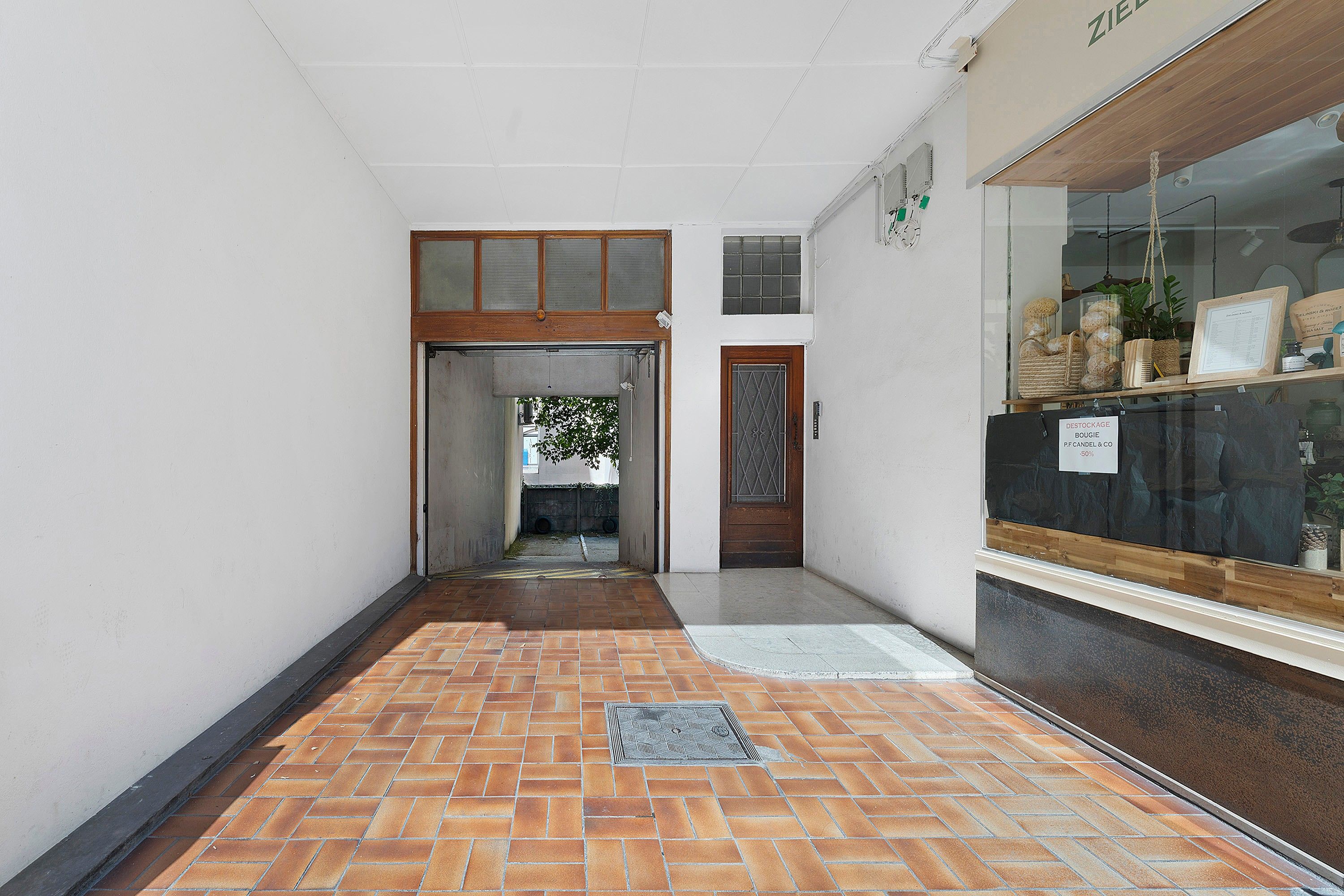 A corridor with a tiled floor, a wooden door, and a reception area with a glass display case.