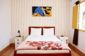 Un dormitorio con cama, mesita de noche, lámpara, un cuadro en la pared y una ventana con cortinas.