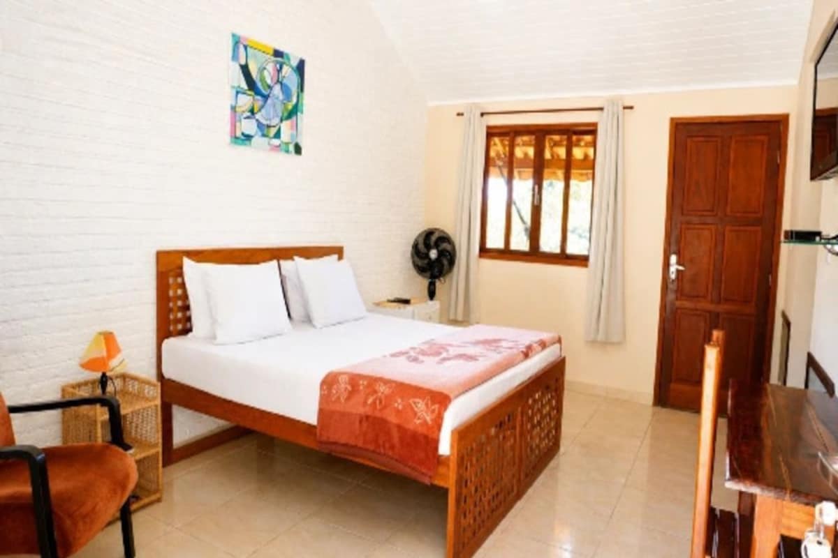 Un dormitorio con cama, una silla, escritorio, ventana con cortinas y una puerta.