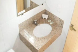 Un baño con encimera de granito, un lavamanos blanco, un espejo y una puerta de madera.