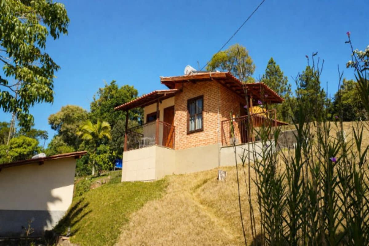 Casa de dos pisos con fachada de ladrillo y techo de tejas, rodeada de follaje y árboles.