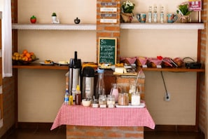 Una barra de desayuno con mantel rojo y blanco a cuadros, una máquina de café y diversos alimentos.