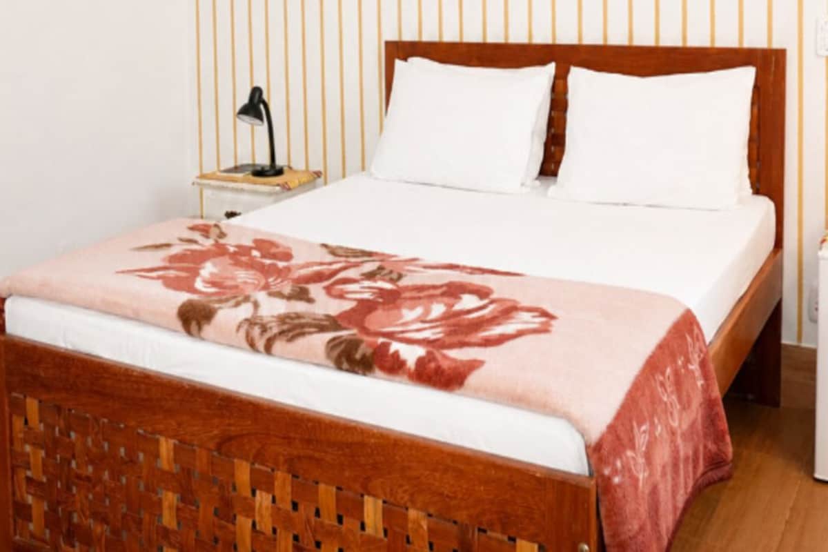 Una cama bien hecha con una colcha floral, un cabecero de madera y una lámpara de noche sobre una mesita.