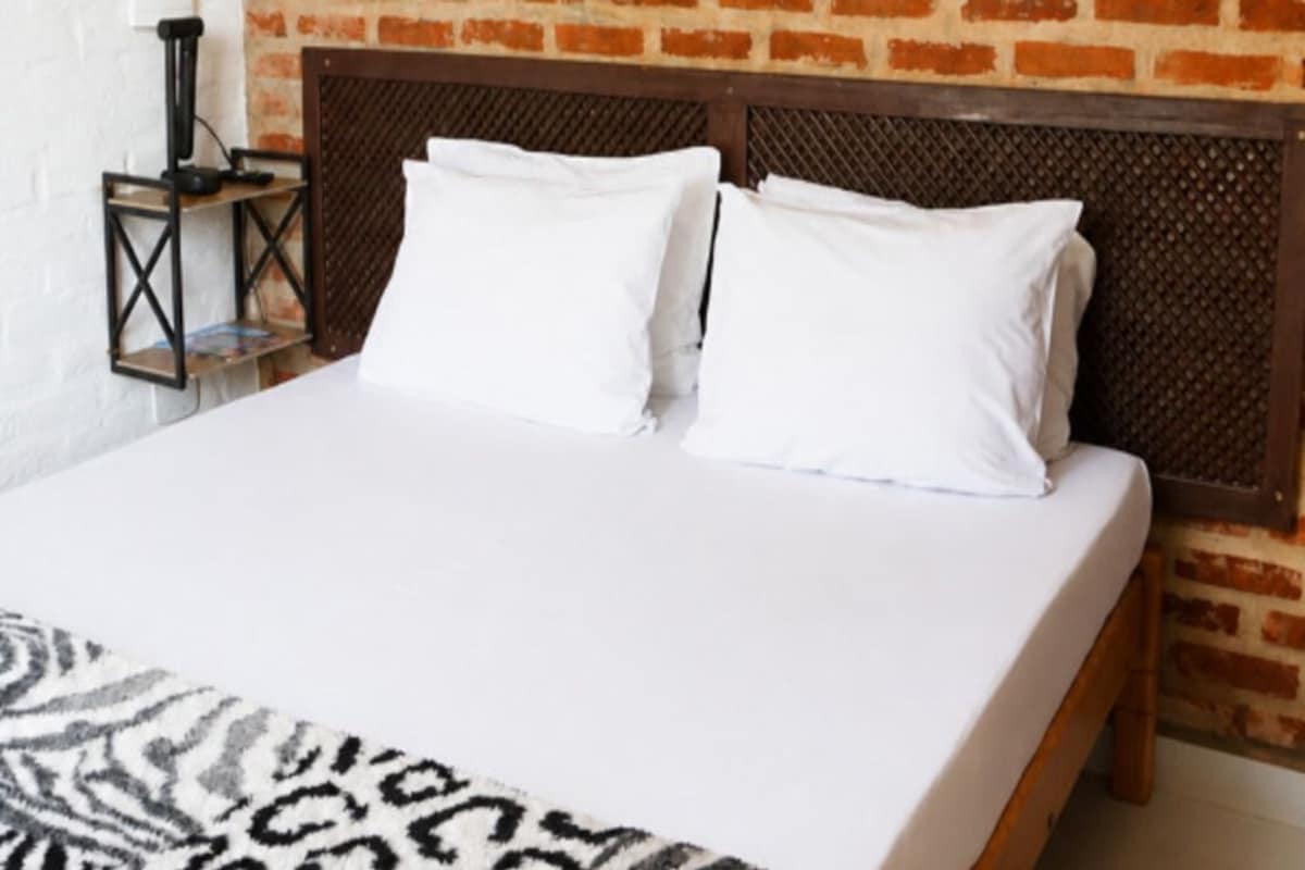 Una cama con ropa blanca, un plaid estampado y un cabecero de madera frente a una pared de ladrillo.