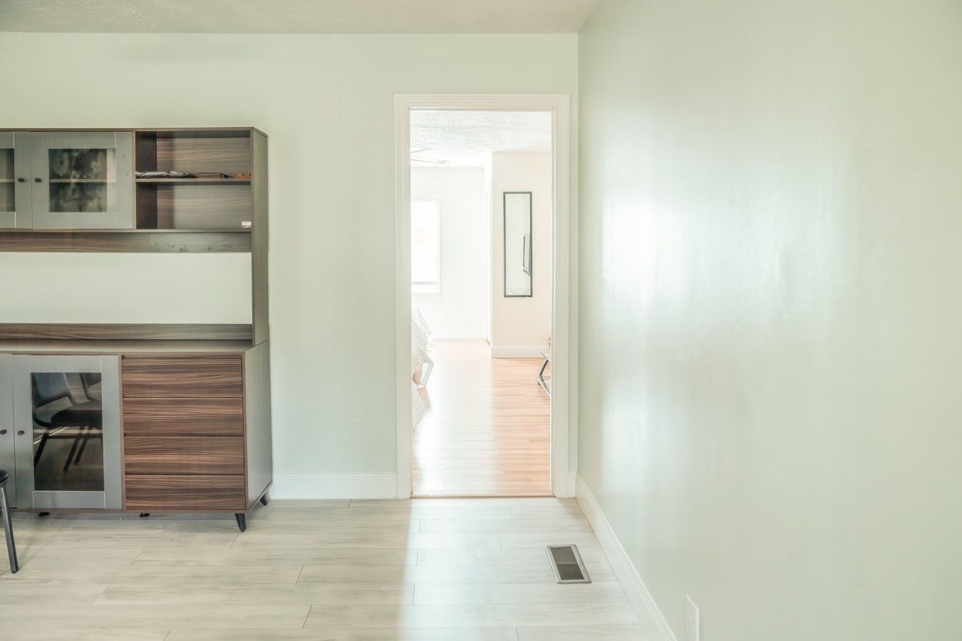 A room with a wooden cabinet, a chair, and a door leading to another room.