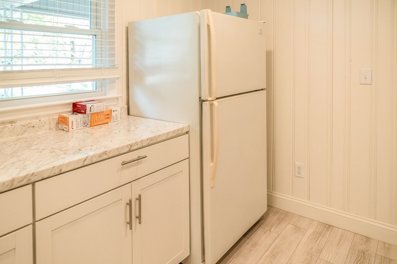A kitchen with a white refrigerator, marble countertop, and white cabinetry.