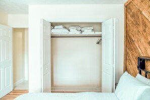 Ett sovrum med en garderob som innehåller hopvikta sängkläder och en vägg med träpanel som fungerar som en dekorativ detalj.