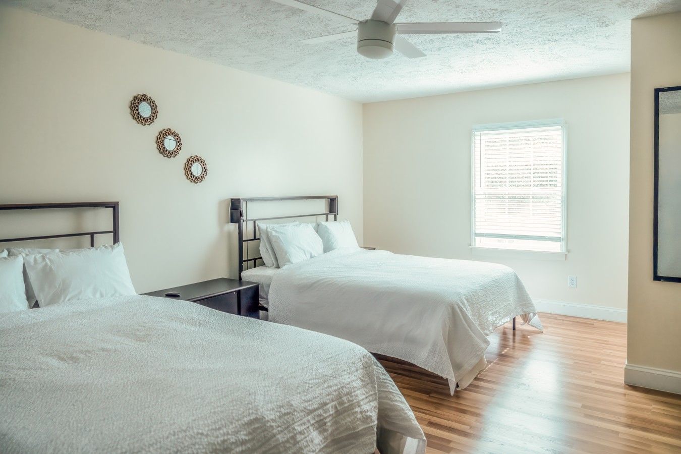 A bedroom with two beds, a ceiling fan, a window with blinds, and a wall-mounted clock.