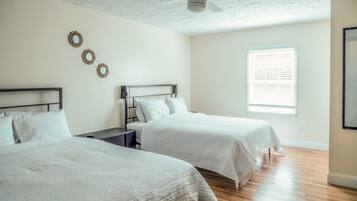 A bedroom with two beds, a ceiling fan, a window with blinds, and a wall-mounted clock.