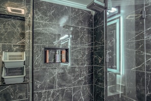 Un baño moderno con cabina de ducha de vidrio, lavamanos integrado y estante con artículos de aseo.
