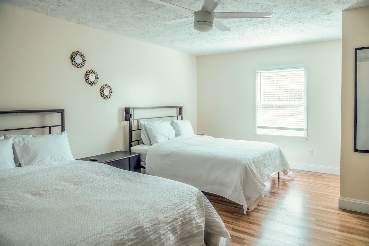 Habitación de hotel con dos camas, un ventilador de techo y una ventana con persianas.