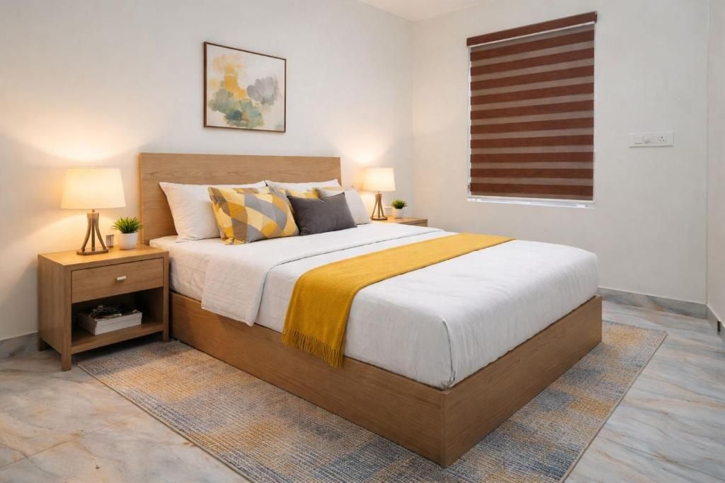 A bedroom with a bed, two bedside tables, a nightstand, a wall-mounted lamp, a window with blinds, and a painting on the wall.
