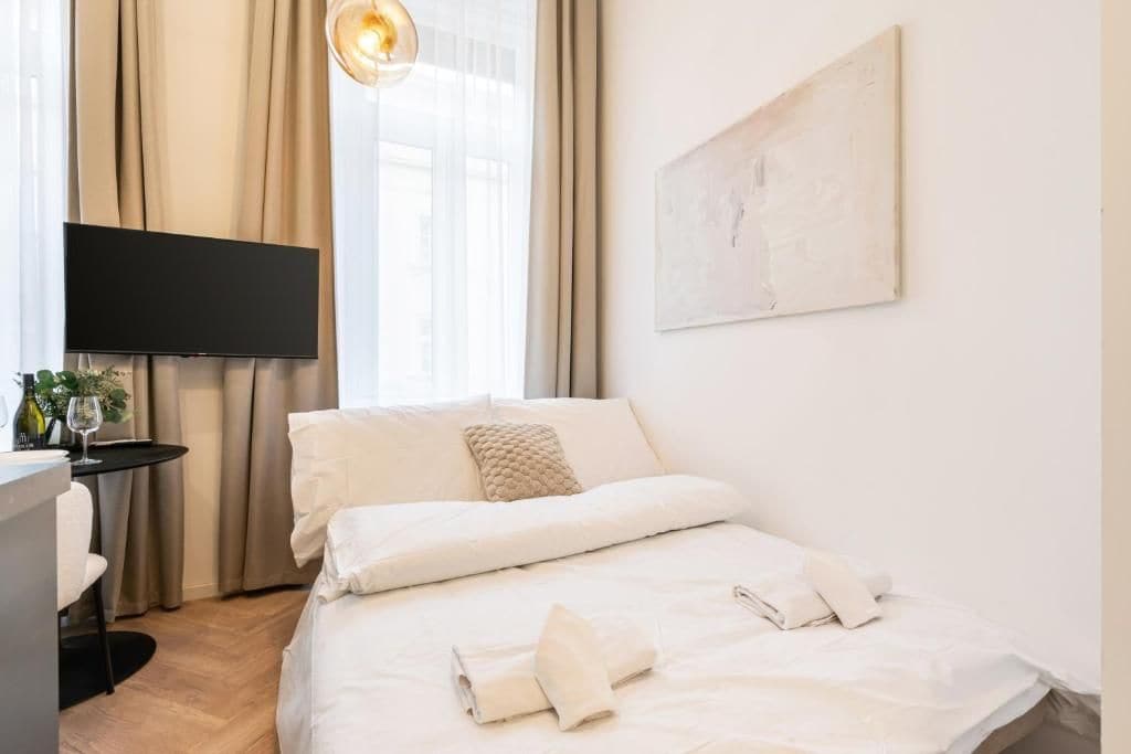 Habitación de hotel con cama, televisor de pantalla plana, una mesita con una planta y un cuadro en la pared.
