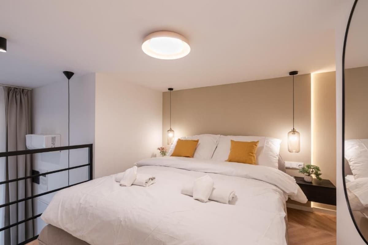 Una habitación de hotel moderna con una cama grande, lámparas de noche y un espejo.