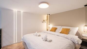 A modern hotel room with a neatly made bed, a hanging light fixture, and a wall-mounted light.
