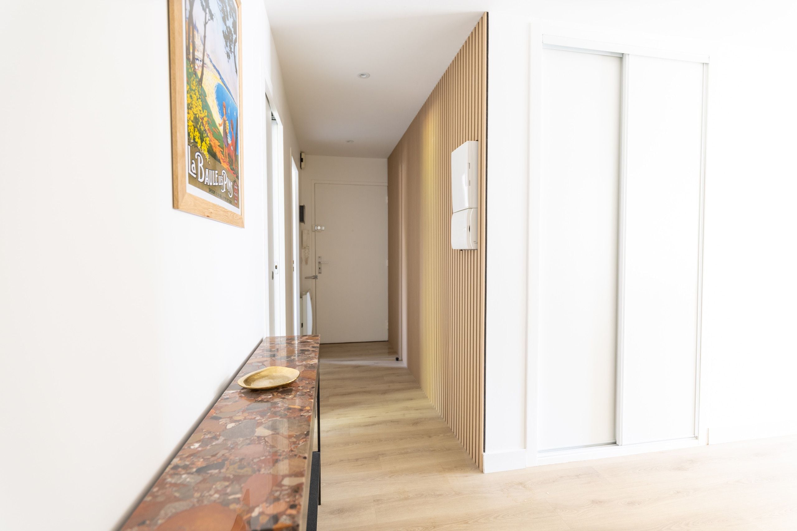 A hallway with a wooden floor, a marble countertop with a plate, and a door with a vertical wooden panel.